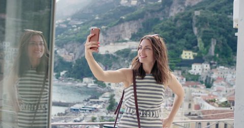 Tourist woman having video chat showing view sharing authentic travel experience from hotel balcony at sunset using smart phone connecting with friends on social media summer vacation in Amalfi Italy