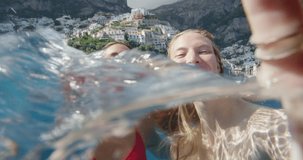 Girl friends taking selfie photograph in water with Positano town in background Tourist women enjoying European summer holiday travel vacation adventure in Amalfi Coast Italy