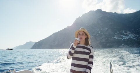 Woman holding alcoholic drink in plastic cup enjoying sunset on party boat European summer holiday travel vacation adventure in Amalfi Coast Italy