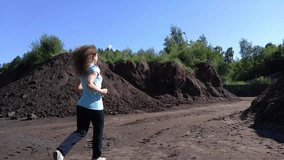 Back of woman in blue shirt running among hills of ground at sunny day, mobile phone video.