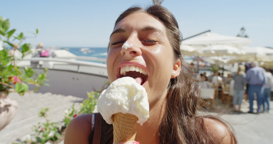Young woman eating ice cream on beach Girl licking Italian Gelato outdoors in summer sunshine enjoying European vacation travel adventure Amalfi Coast Positano Italy