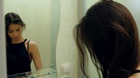Beautiful brunette girl drying her hair and looking in the mirror in her bathroom