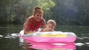 Little baby and grandma swimming in a lake on inflatable mattress in sunny day in summer in slow motion. 1920x1080