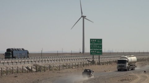 YUMEN - SEPTEMBER 2 2010: A truck drives over a sandy road next to a highway and windmill in Western China