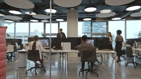 PAN of busy businesspeople working in modern office space with glass walls and panoramic windows