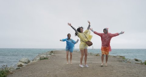 Diverse group of friends dancing freestyle silly dance in rainy weather on the beach celebrating adventure