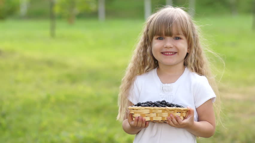 Laughing child holding a basket of black currant.
