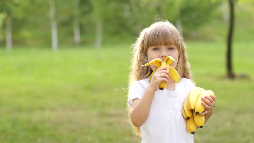Girl eating a banana and smiles.
