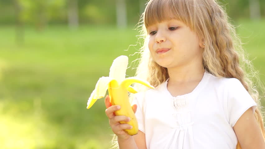 Girl eating a banana and smiles. Thumbs up
