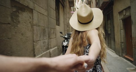 Young couple holding hands woman leading boyfriend walking down European street in Barcelona Spain POV travel concept