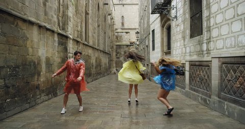 Diverse group of friends dancing freestyle in European City wearing multi colored poncho rain coats in rainy weather celebrating travel adventure