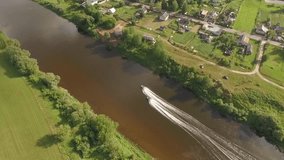 Video footage taken from bird's eye view by drone of floating speed boat on river in countryside. View from the top to the wide river,forest, large fields on sunny day. High speed boat video on river.