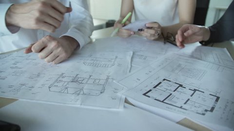 Close up hands of three workers discussing building drawings in office. Closeup shooting of arms moving pictures, watching attentively on images. design drafts for construction of large sports complex