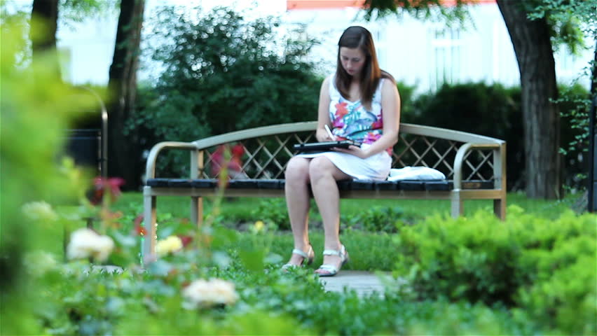 Young happy woman with tablet computer sitting in the park