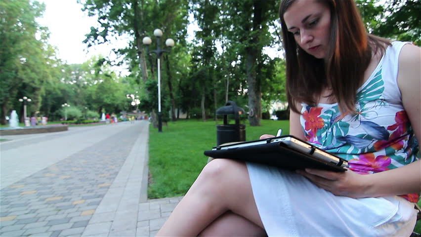 Young happy woman with tablet computer sitting in the park