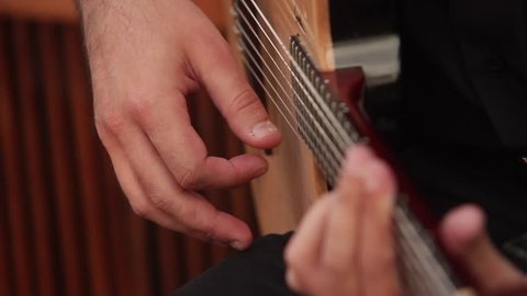Close-up view of male hands playing acoustic guitar with a mediator.