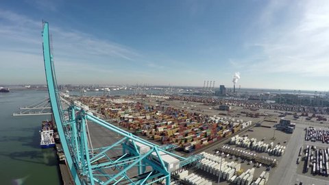 Aerial bird view flying over harbor area past blue harbour cranes for loading or unloading intermodal containers in background a container terminal with containers ready for transport blue sky 4k