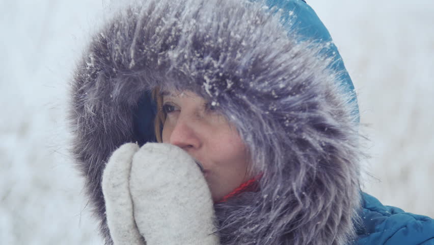 A nice girl in mittens drinks and warms herself with hot tea in a winter park.