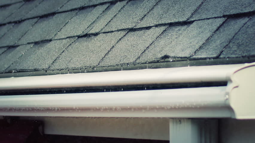 Close-up of rain falling on and rolling off a roof and gutter on a house.