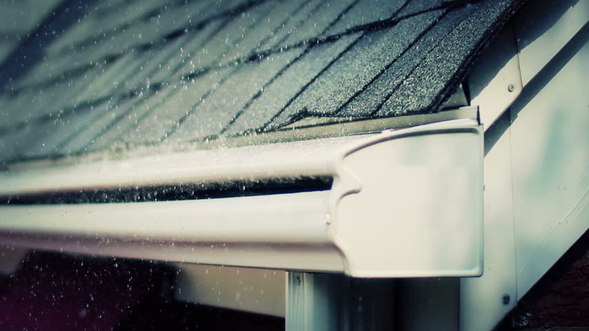 Close-up of rain falling on and rolling off a roof and gutter on a house.
