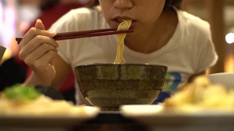 4K Asian woman eating beef noodles for dinner in a restaurant. Using sticks for eat the hot traditional chinese food-Dan