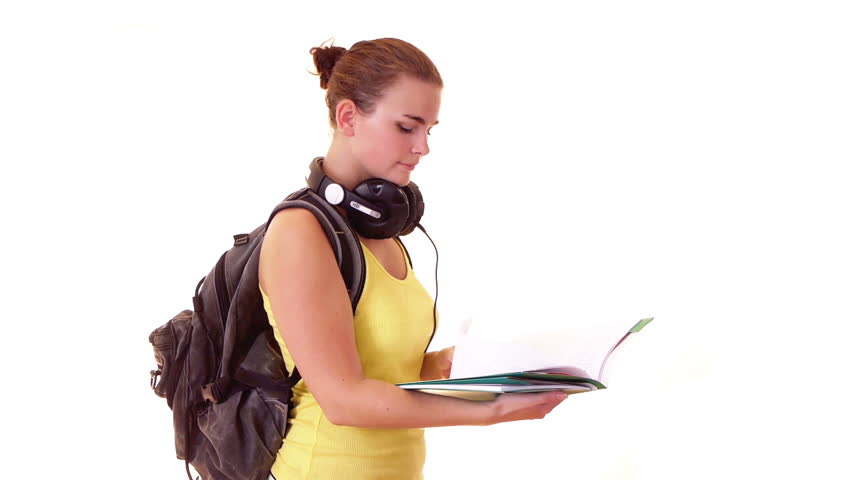 Student with headphones and backpack reading something in textbook 

