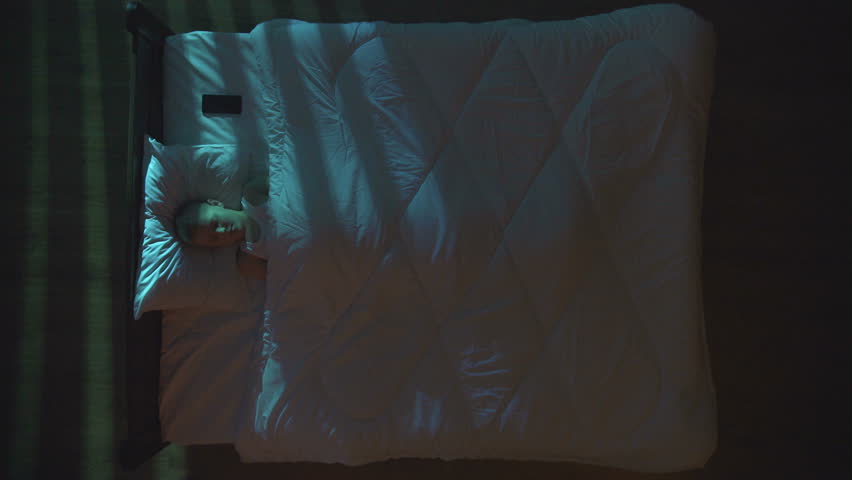 The sleeping boy lay on the bed and phone. Evening night time. View from above
