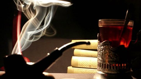 Tobacco pipe sits on the desk beside a glass of tea and a stack of books