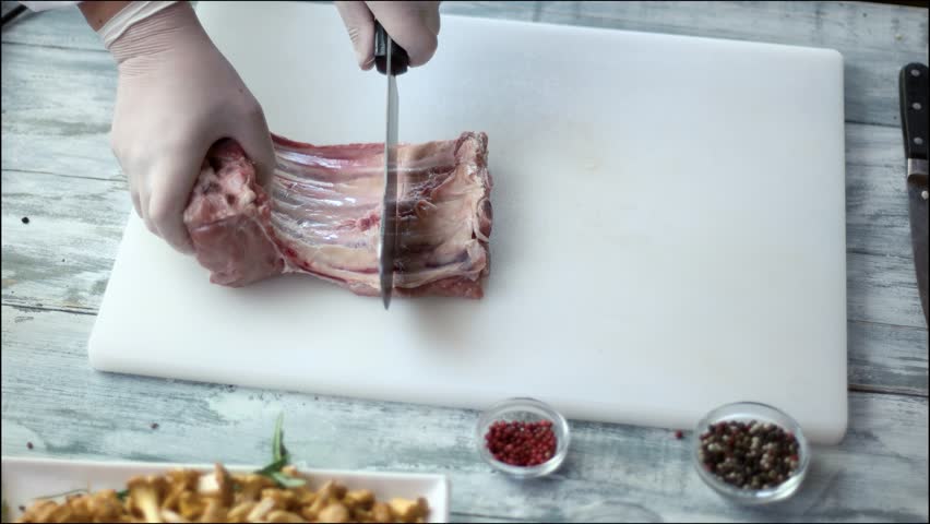 Hand cutting meat with cleaver. Gray wooden cooking table.