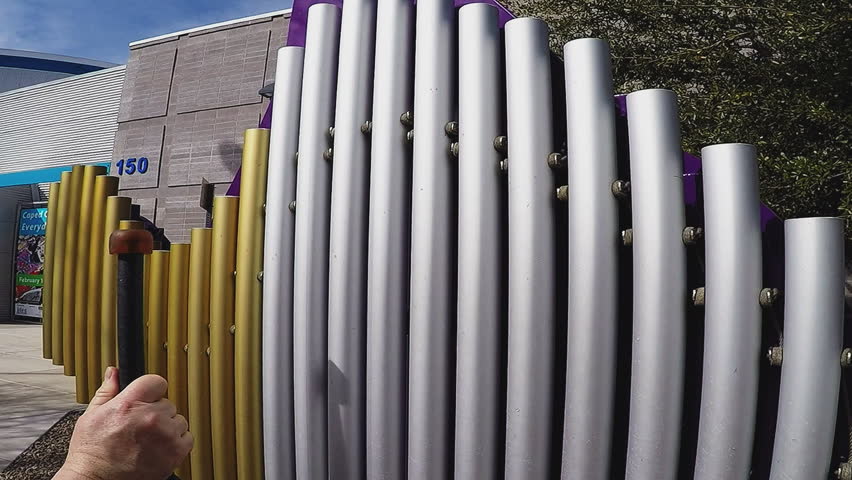 MESA, AZ/USA: February 22, 2017- A man strikes a xylophone creating musical tones. Close up shot of a hand and mallet creating sound on hanging metal tubes.