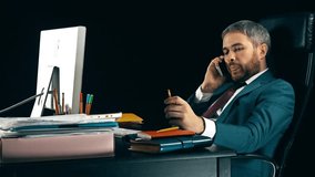 Bearded businessman talking on his cell phone. Dark background, isolated. 4K video