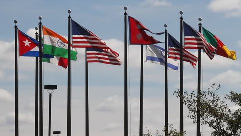 The flags US, Nepal, Cameroon,  Israel, India, Mexico and Cuba on a flagpoles blowing in the wind against a blue sky and white clouds. Flags of various countries fluttering in the wind on a flagpoles.