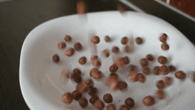 chocolate cereal balls in white bowl for breakfast, close-up video in motion, slow motion