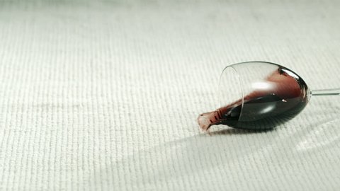 wineglass with red wine tipping over, spilling on white napkin