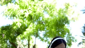 Asian woman listening to the music from a smart phone with headphones in a park