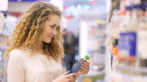 Cute 20s blonde lady with long curly hair make purchases in department store close up. Young mother select puree and juices for child, putting food in basket holding hand. Concept of caring for a baby