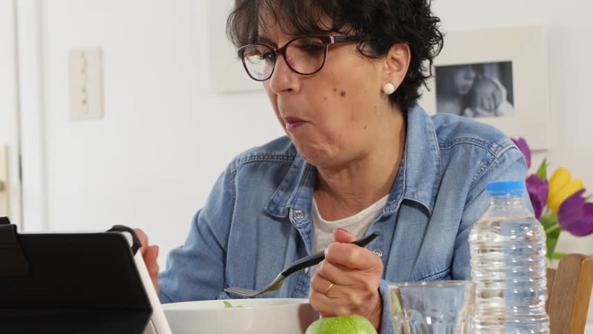 Mature woman looking digital tablet while eating a salad | Shutterstock HD Video #25011752