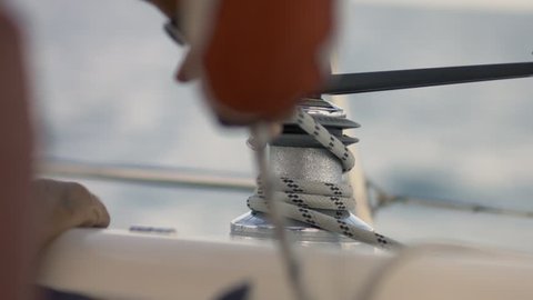 Hands pulling ropes, winding sheets around winches on yacht