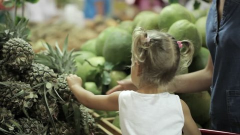 Young mother and little cute daughter selecting fruits at the supermarket