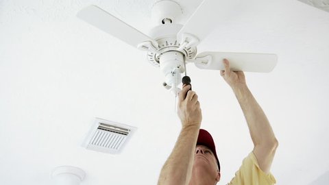 An electrician or homeowner handyman type installing the blades of a ceiling fan.