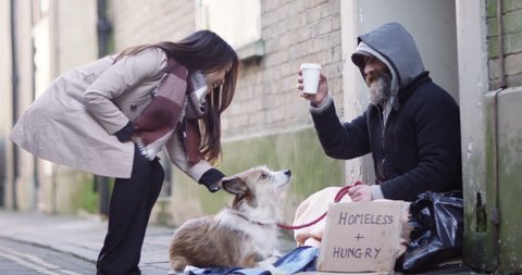 4k, A young woman offering a cup of coffee to a homeless person sitting outside in cold.