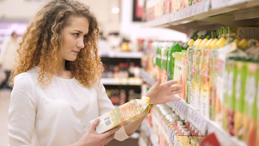 Woman chooses juice in the supermarket. Shopping in the store. Young female carefully analyzing products in a market. Shopping in Grocery Store or Supermarket