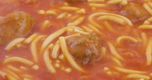 Canned spaghetti and meatballs in a skillet simmering the stirring the food as it cooks with bubbles and steam rising.