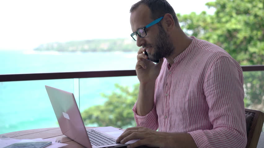 Young man talking on cellphone and drinking water sitting on terrace 
