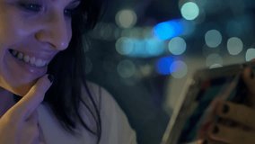 Happy, young woman watching movie on smartphone by window at night
