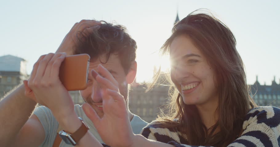 Tourist couple taking selfie photograph with smartphone in city at sunset sharing lifestyle photo enjoying holiday European vacation travel adventure London