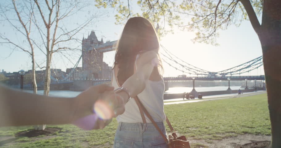 Young couple holding hands woman leading boyfriends walking towards Tower Bridge London POV travel concept