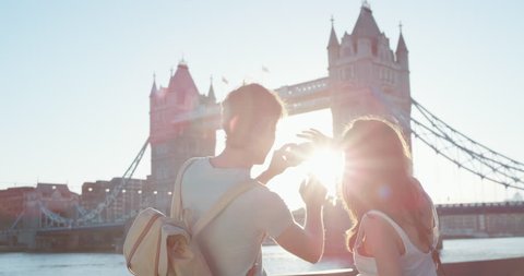 Tourist couple taking photograph of tower bridge London using smartphone photographing scenic cityscape view enjoying vacation travel adventure