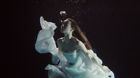 young woman swimming under the water on a black background