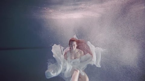 young woman with long red hair swimming underwater like a fairy tale